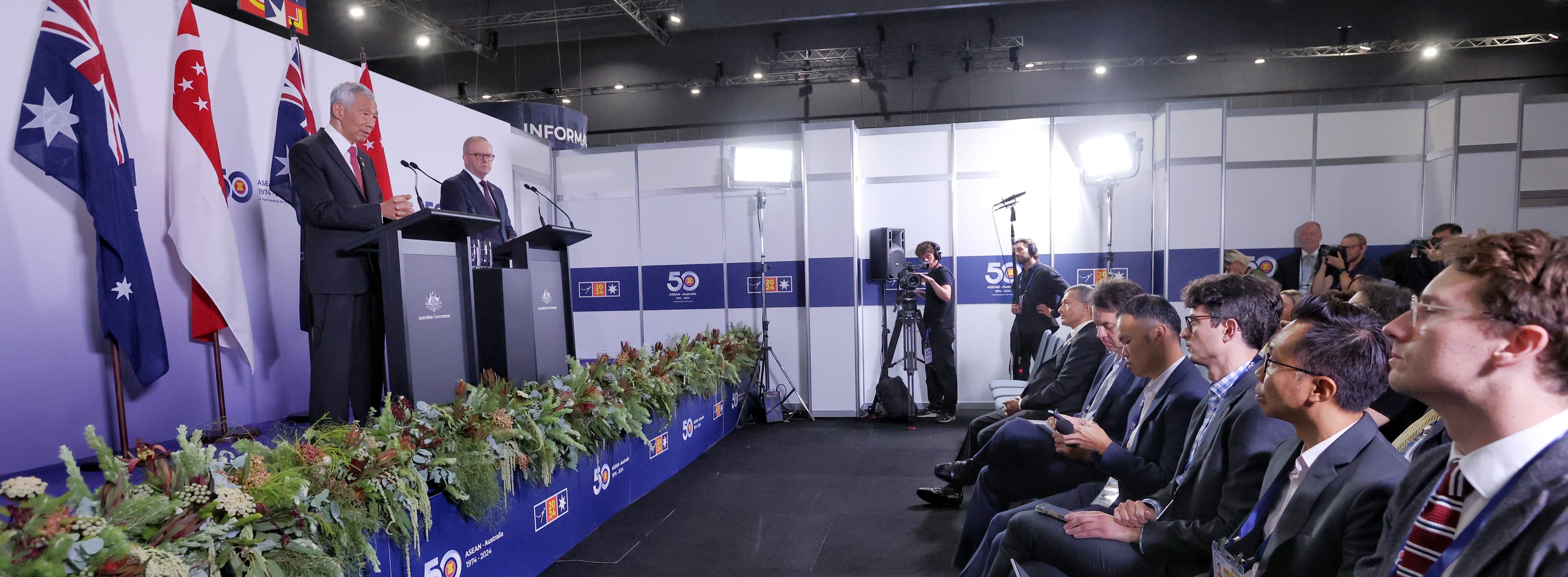 Two men at podiums with flags and audience. "Australian Government" logo shown.